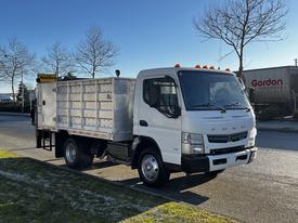 A 2014 Mitsubishi Fuso FE truck with a flatbed and side walls is parked on the street with its headlights on