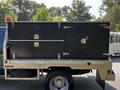 A 2008 Ford F-550 with a metal storage compartment mounted on the flatbed featuring multiple locked sections and handles