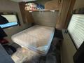 A 2014 Launch 24RLS camper interior featuring a bare mattress on a bed frame with a pillow and bright patterned blanket stored above in a shelf