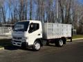 A white 2014 Mitsubishi Fuso FE truck with a flatbed and metal sides is parked, showcasing its front and side view