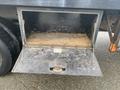 A close-up view of an open storage compartment under a truck bed revealing a wooden floor with some dirt and wear