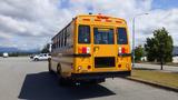 A yellow 2014 Freightliner Thomas bus with a diesel engine parked with its rear facing the viewer showcasing emergency lights and large windows