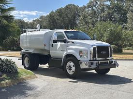 A white 2016 Ford F-750 truck with a water tank attached and a black grille is parked on a street