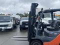 A 2011 Toyota 028FG15 forklift with a black frame and orange accents, featuring two long forks extending from the front for lifting heavy loads