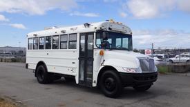 A white 2015 International PC105 bus with a black front bumper and large windows, featuring a door on the driver's side and multiple lights on the roof