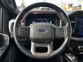 A black leather steering wheel of a 2021 Ford F-150 featuring control buttons and a Ford logo in the center