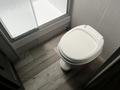 A white toilet installed in a corner of a bathroom with a glass shower enclosure nearby