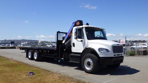 A 2017 Freightliner M2 106 flatbed truck with a crane attachment on the side parked on a paved area