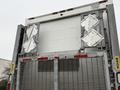 The rear of a 2017 Kenworth T370 truck with a roll-up door and metal grating featuring folding ramps on each side designed for loading and unloading cargo