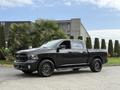 A black 2018 RAM 1500 pickup truck with large black wheels and a chrome step rail parked in a well-maintained area with greenery around it