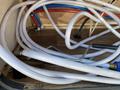 White hoses with blue and red connectors are coiled on a wooden surface inside the compartment of a 2016 Jayco 265RLSW camper