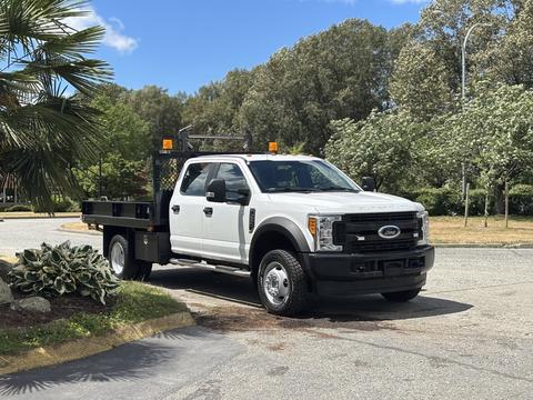 A white 2017 Ford F-550 truck with a flatbed and warning lights parked on a roadway