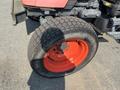 A close-up of a rear wheel of a 2010 Kubota M6040 tractor featuring a thick rubber tire with a rugged tread and a bright orange wheel rim