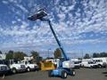 A blue 1997 Genie S-65 4X4 aerial lift with a raised platform and large wheels positioned in a vehicle yard