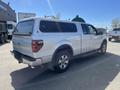 A 2014 Ford F-150 pickup truck in white with a covered bed and chrome wheels is parked at an outdoor location