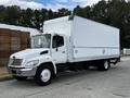 A 2006 Hino 268 truck with a white box cargo area and a shiny front grille parked on a paved surface