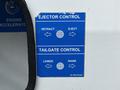 A blue control panel on a vehicle featuring instructions for ejector and tailgate controls with arrows indicating directions for retract and lower