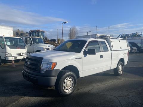 A 2013 Ford F-150 in white with a tool box in the truck bed and black bumpers parked on a lot