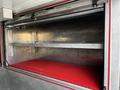 A red rubber mat covers the bottom of an open compartment inside a 1994 Freightliner FL80 with two metal shelves on the top