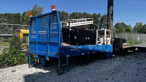 A 2000 flat deck 18 foot trailer with a blue frame and orange safety lights on top positioned at an angle with equipment on the deck