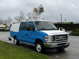 A 2009 Ford Econoline van painted blue and white with a raised platform on top and equipment attached for aerial access