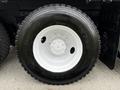 A close-up view of a black truck tire mounted on a white wheel with five spokes and a central hub on a Freightliner M2 112