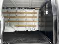 Interior view of a 2023 GMC Savana cargo van featuring wooden storage shelves and a black partition on one side with rubber flooring