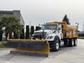 A 2016 International 7600 truck with a yellow and black snow plow blade attached to the front and a yellow spreader in the back