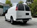 A white 2023 GMC Savana van viewed from the rear with a smooth body and no rear license plate, featuring red taillights and chrome accents on the bumpers