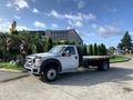 A white 2013 Ford F-450 Super Duty flatbed truck parked on a driveway with a flat cargo area and visible front grille