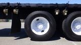 A close-up of a black Freightliner M2 106 truck's wheel with a white rim and visible tire tread mounted on a flatbed trailer