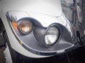 Close-up of the front driver's side headlight and turn signal of a white 2012 International 7300 Workstar truck with a shiny chrome trim and raindrops on the surface