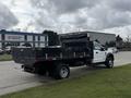 A white 2021 Ford F600 truck with a flatbed and black sides parked on a street.