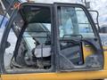 A 2018 John Deere 350 excavator cab with a large front window open showing the operator's seat and controls inside