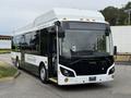 A 2018 Grande West Vicinity bus with a sleek design featuring large windows and a white and green color scheme, parked with the driver’s door open