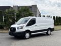 A 2023 Ford Transit van with a white exterior and black trim parked at an angle with a roof rack and steel wheels