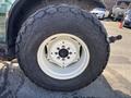A large rear tire of a 2010 New Holland T4050 tractor showing deep treads and a white wheel rim with visible rust around the bolts