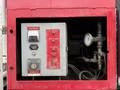 A red control panel featuring a voltmeter test flow switch fuel valve and a pressure gauge with various knobs and switches