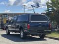 A 2014 Ford F-250 SD pickup truck with a cap on the bed parked on a lot showing a dark exterior and chrome wheels