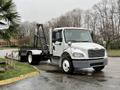 A white 2019 Freightliner M2 truck with a flatbed and a black lift gate parked on a wet surface