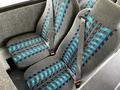 Two padded bus seats with blue and teal stripes and seat belts each featuring a design of interwoven patterns