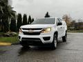 A white 2018 Chevrolet Colorado pickup truck is parked with its front angled slightly towards the viewer showcasing its distinctive Chevrolet bowtie emblem on the grille