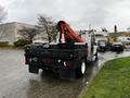 A 2014 Ford F-550 work truck with a red crane attachment on the back and a black flatbed, parked in a lot with wet pavement