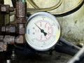 A round pressure gauge with a white dial displaying measurements in kilopascals and psi surrounded by metal valves and tubing