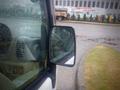 A close-up of the side mirror of a 2003 Toyota Toyoace showing droplets of rain on the glass