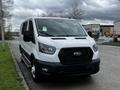 A white 2023 Ford Transit van is parked, featuring a black grille, large headlights, and a streamlined design with sliding side doors and a high roof