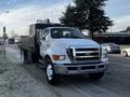 A 2011 Ford F-750 with a flatbed design and a large cab is parked on the street the vehicle features a white exterior and front grille with visible headlights