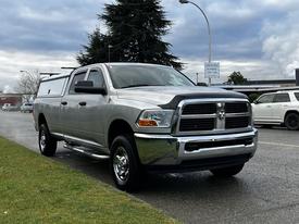 A silver 2012 RAM 3500 pickup truck with chrome accents and a truck bed cover parked on the street