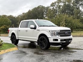 A white 2018 Ford F-150 with black wheels parked on a wet surface showcasing its sleek design and modern pickup features