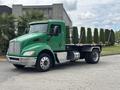 A green 2013 Kenworth T370 truck with a flatbed and no cargo featuring large front headlights and a distinctive grille design